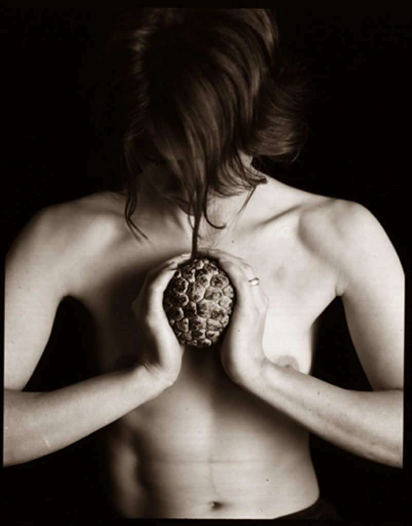 Black and white photo of topless woman holding fruit