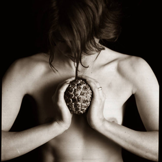 Sepia toned photograph of topless woman holding large seed pod