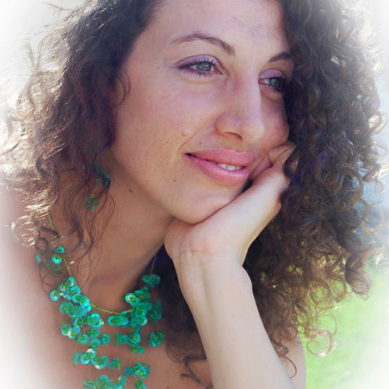 Color photograph framed in oval of curly haired woman with green necklace
