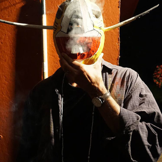Color photograph of man holding mask up to face with smoke blowing out