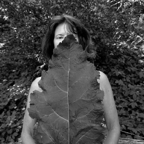 Black and white photograph of woman holding large leaf in front of body